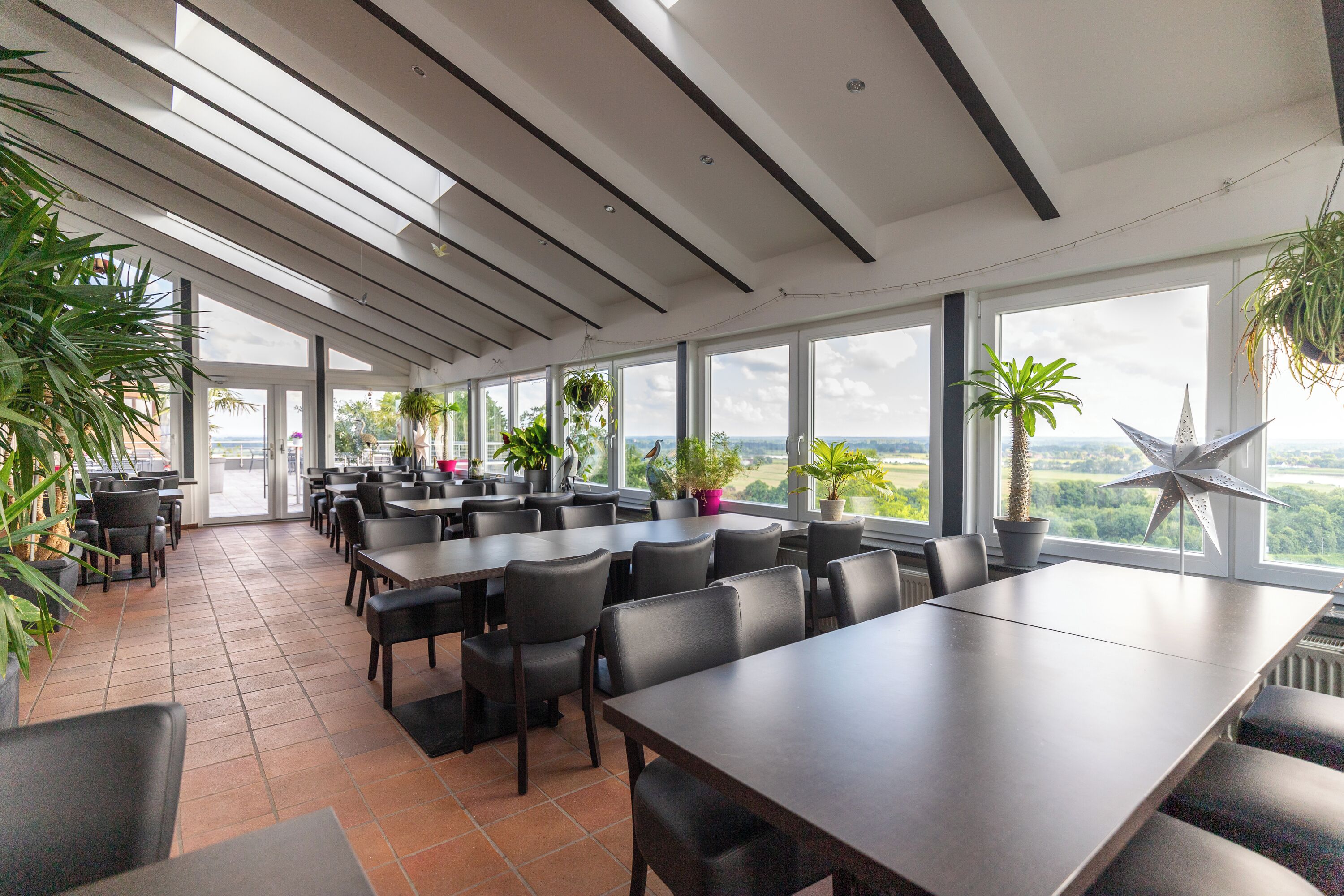 Un comedor moderno con ventanas amplias, sillas negras y plantas en macetas.