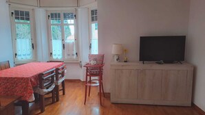 A room with a wooden dining table, a red chair, a television on a cabinet, and a window with a view of trees. - B&B Brunate Kangucavallo (Brunate)