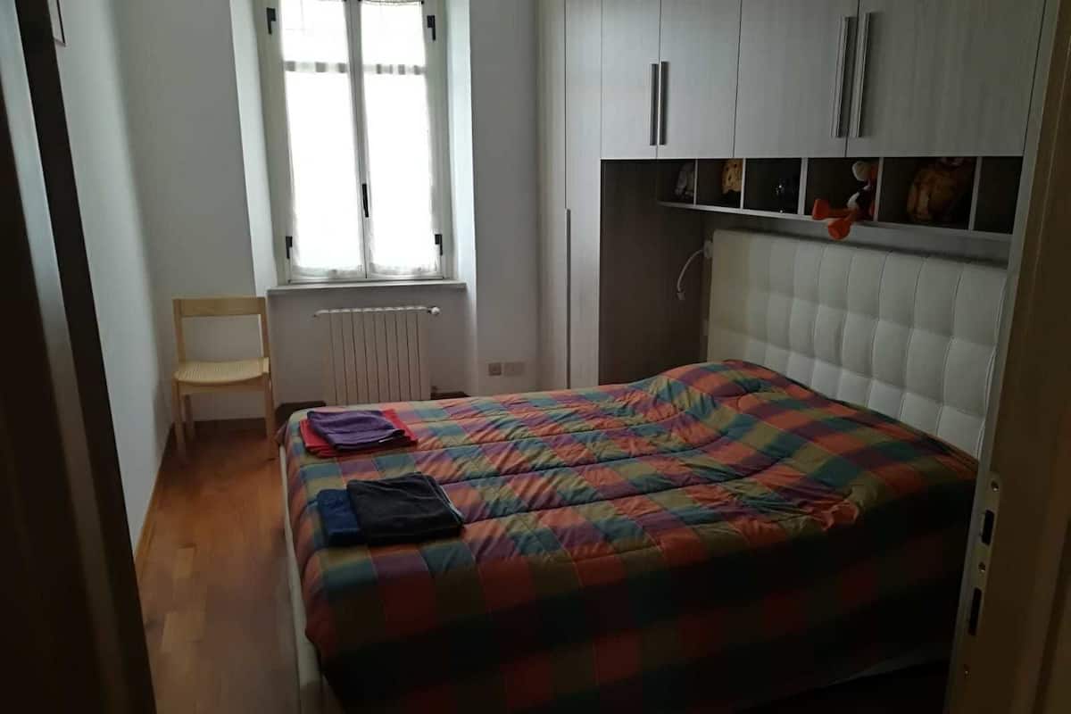 A bedroom with a bed, a chair, a radiator, and a window.