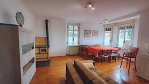 A cozy living room with a sofa, a dining table, and a kitchen area with a stove. - B&B Brunate Kangucavallo (Brunate)