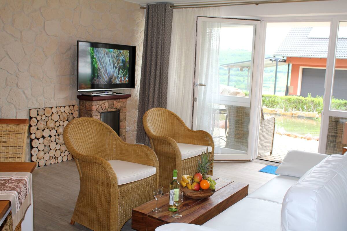 A living room with wicker chairs, a flat-screen TV, a fireplace, and a fruit bowl on a wooden table.