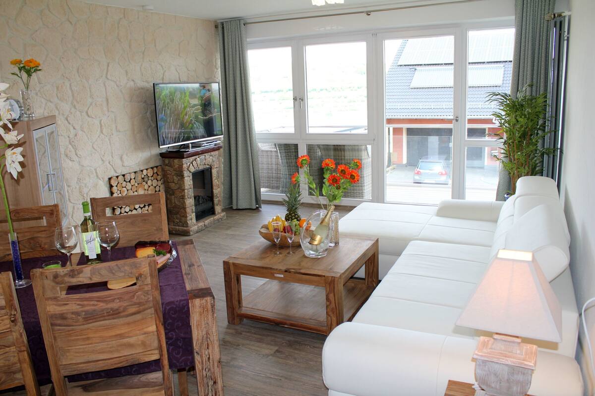 A living room with a TV, wooden furniture, a white sofa, and a view of the outside.