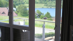 A room with a view of a lake and greenery. - Ferienwohnungen Maarberg Resort (Schalkenmehren)
