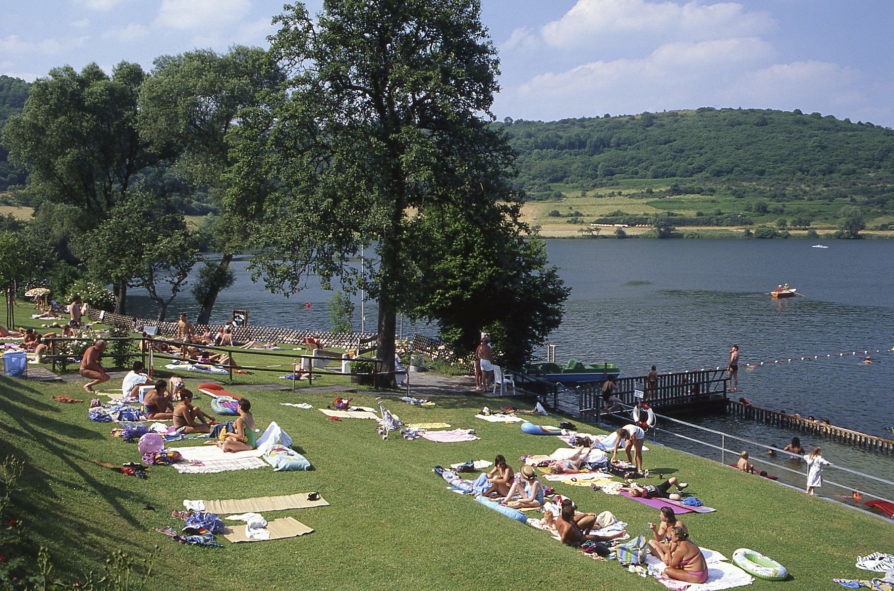 Ein Park am Seeufer mit Rasenflächen, Picknicktischen und einem Steg, der ins Wasser ragt.