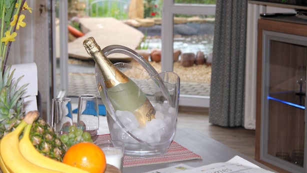 A table with a bottle of champagne in a glass bowl, surrounded by fruits and glasses. - Ferienwohnungen Maarberg Resort (Schalkenmehren)