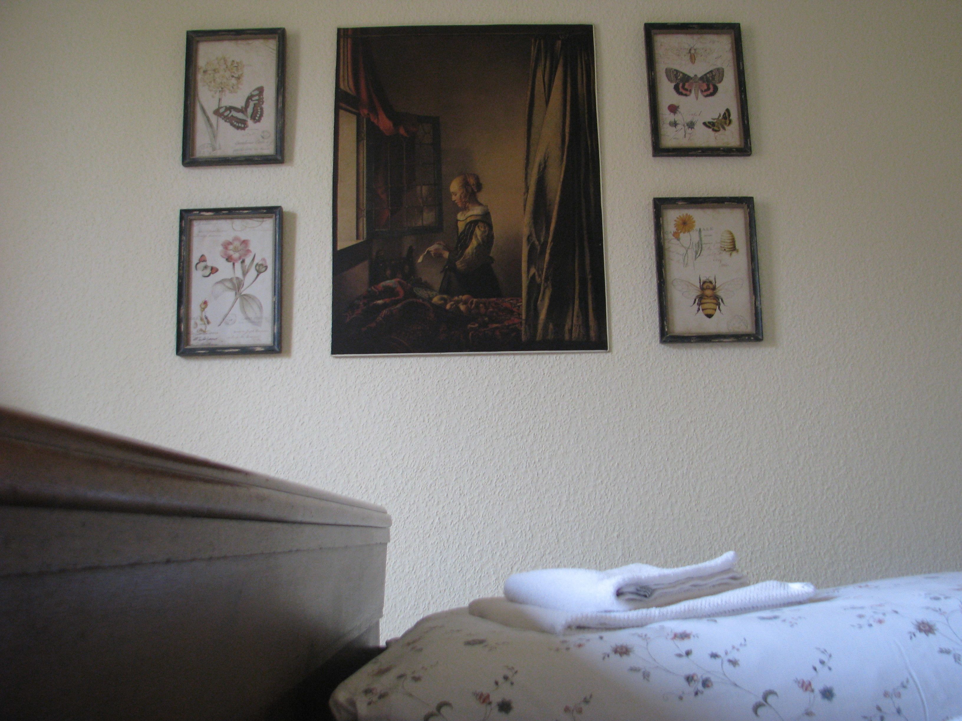 A bedroom with a bed, a nightstand, and a wall with framed pictures.