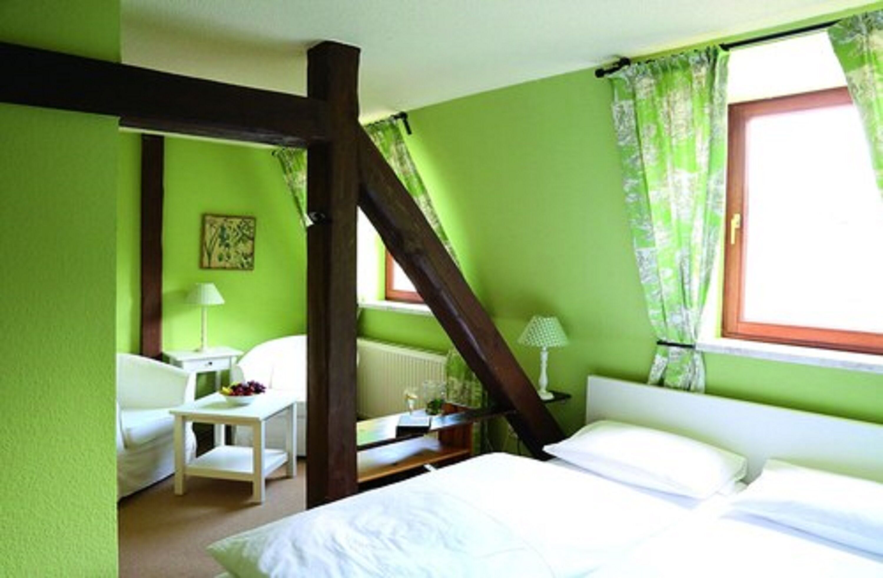 Una habitación con cama, una silla, una mesita y una ventana con cortinas.