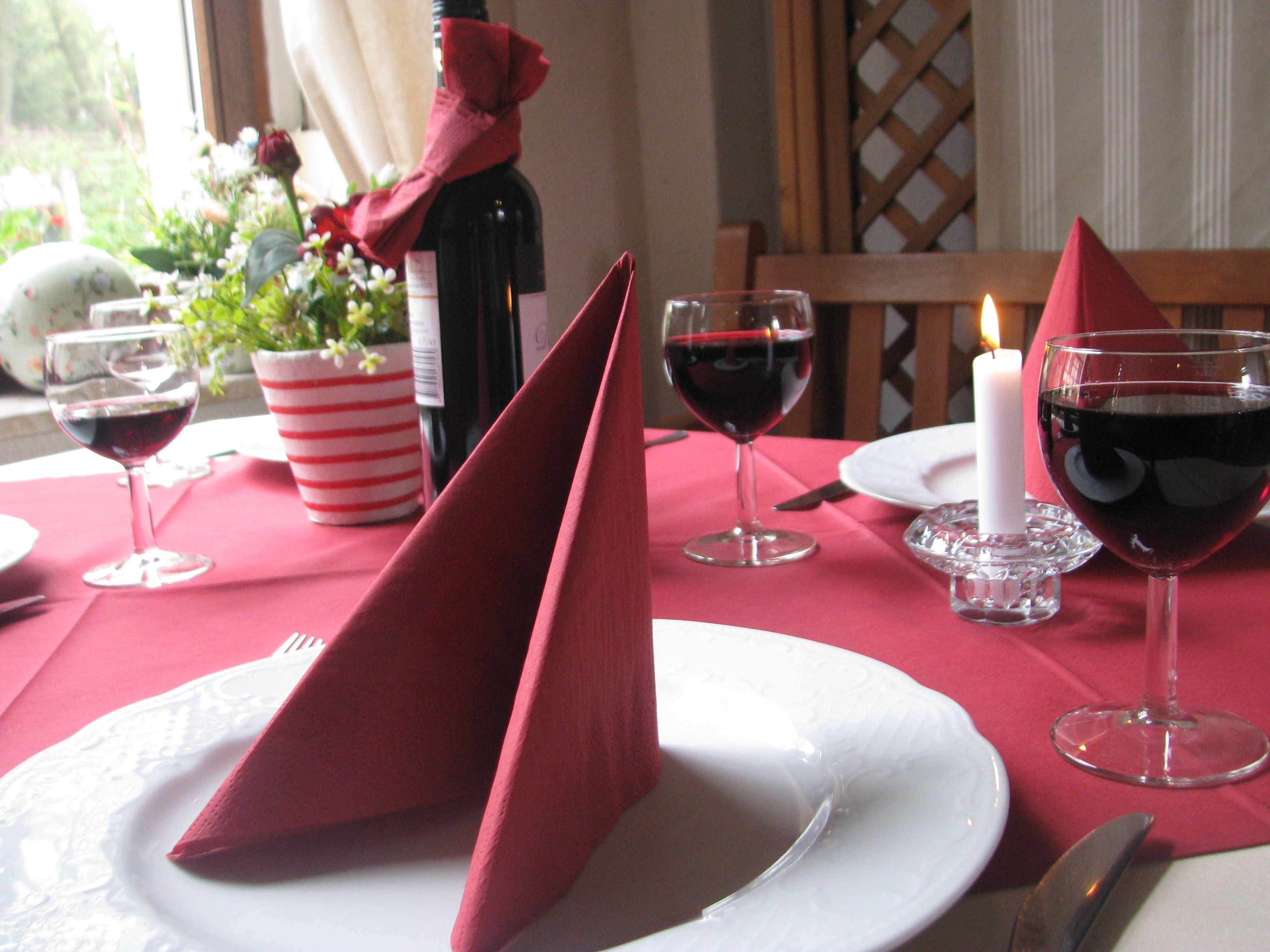 A table set with red napkins, wine glasses, a candle, and a bottle of wine.