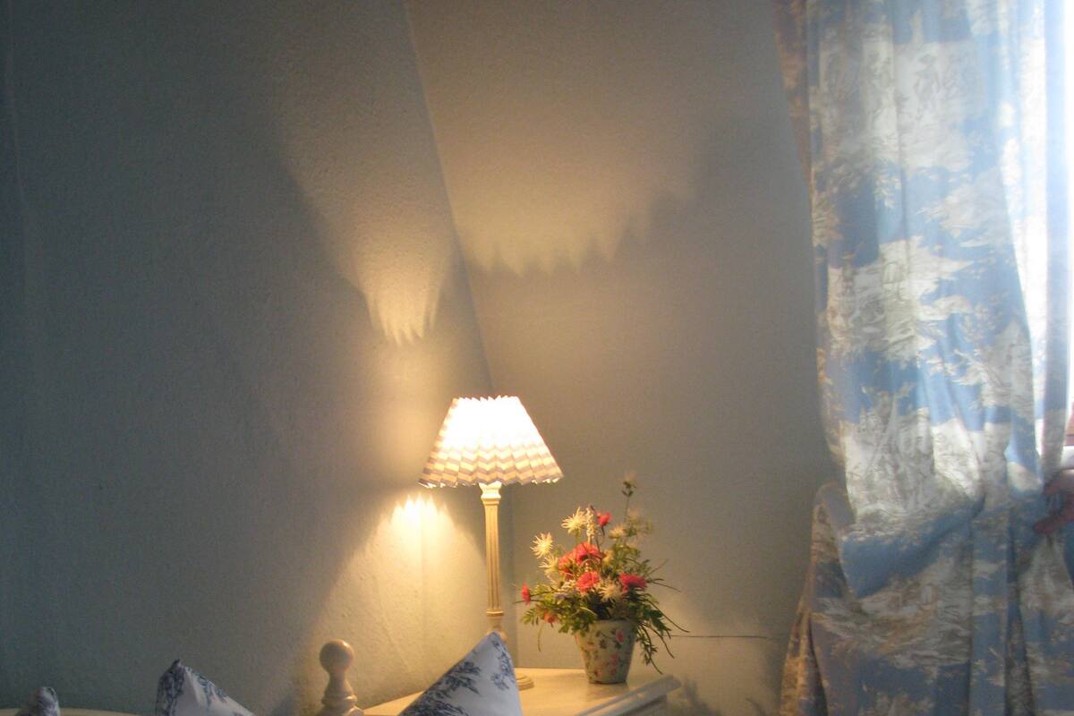 Une chambre à coucher avec un lit, des oreillers, une table de chevet, une lampe et un vase rempli de fleurs.