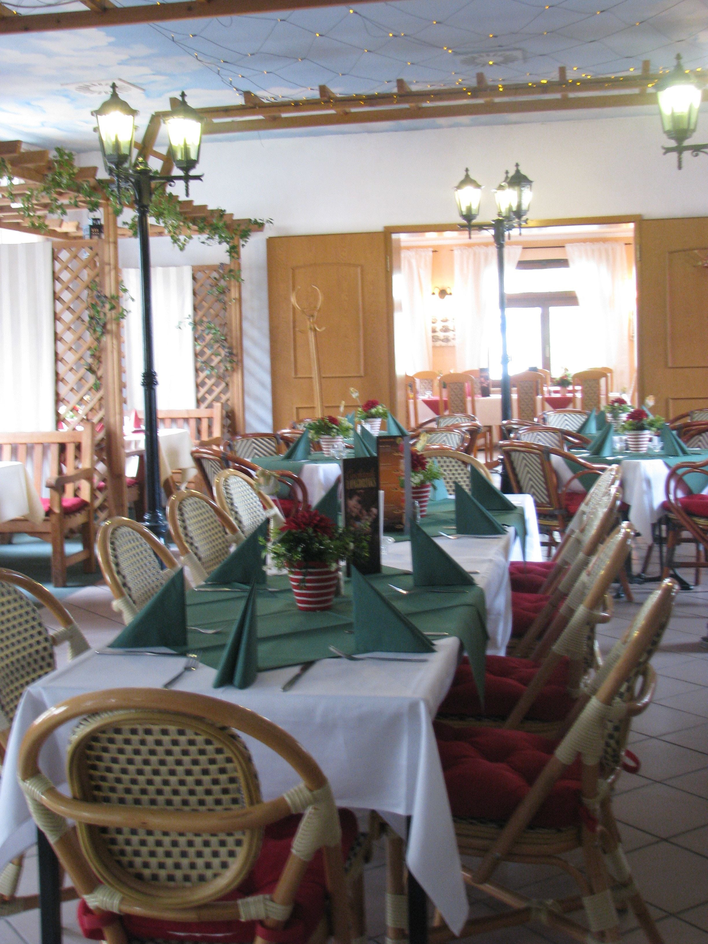 A restaurant with wooden chairs, tables with green tablecloths, and hanging lanterns.