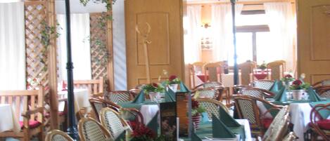 A restaurant with wooden chairs, tables with green tablecloths, and hanging lanterns.