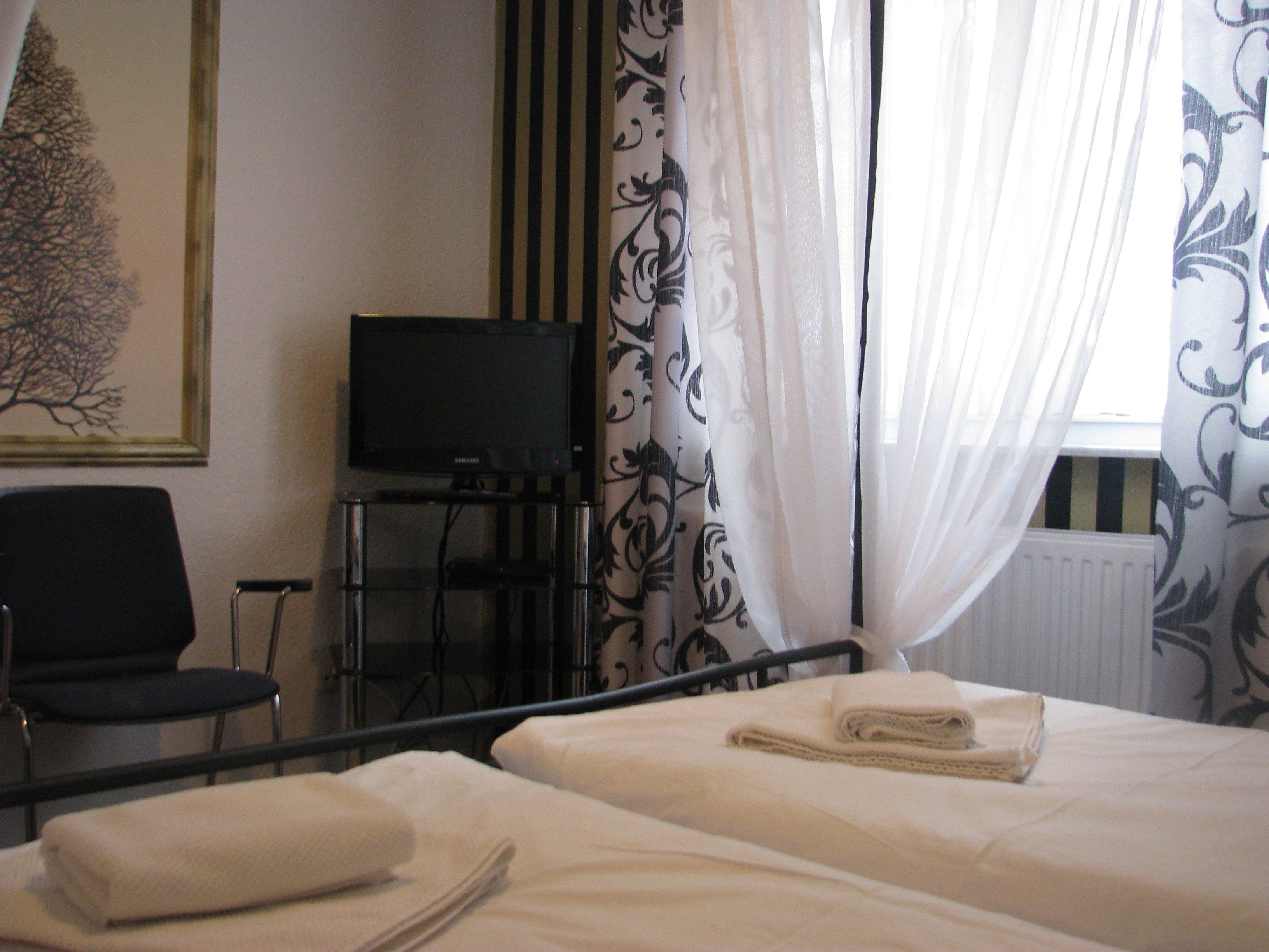 A hotel room with a bed, a chair, a television, and a window with curtains.
