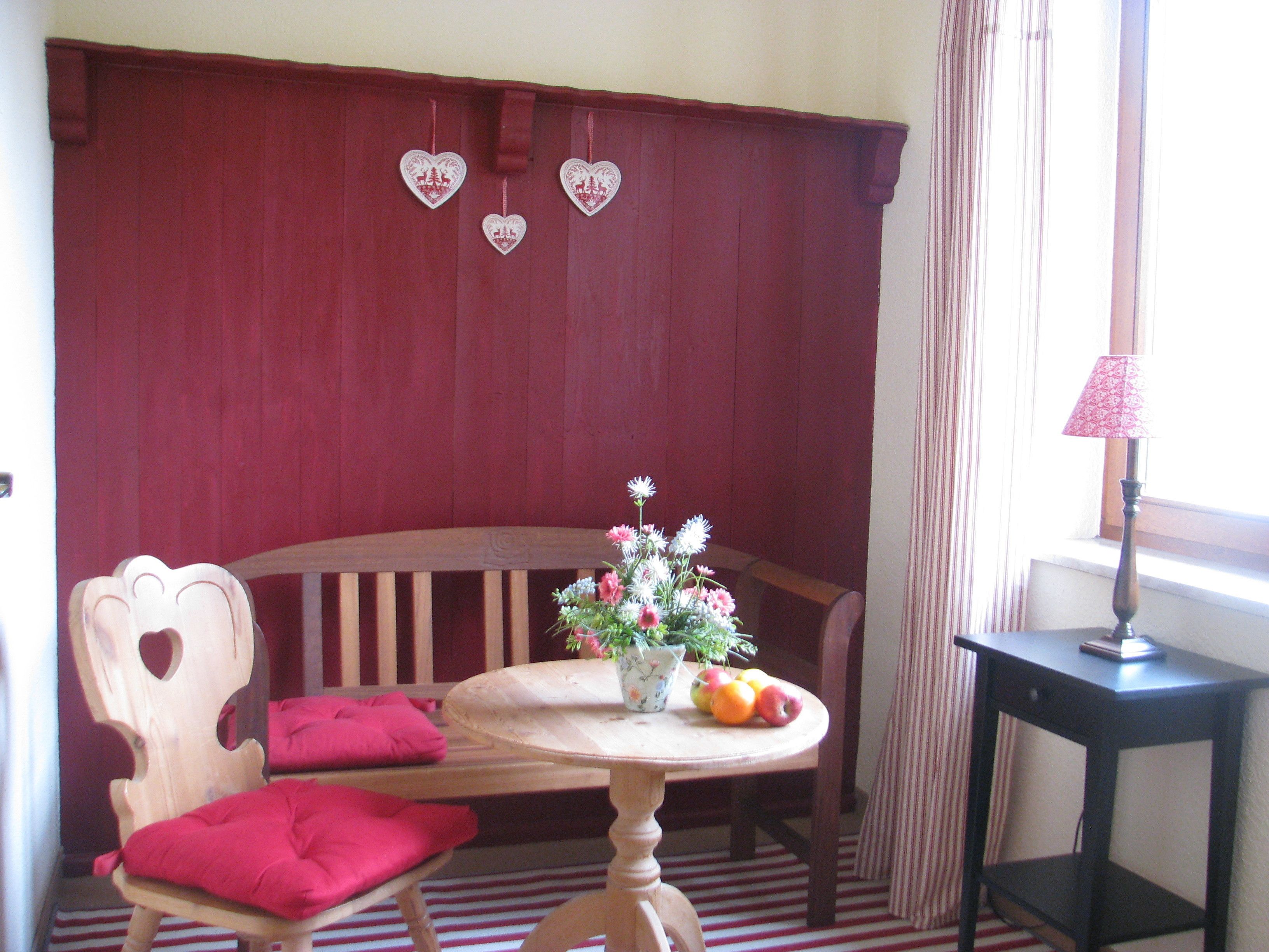 A room with a wooden bench, a table with a vase of flowers and fruit, and a lamp on a side table.