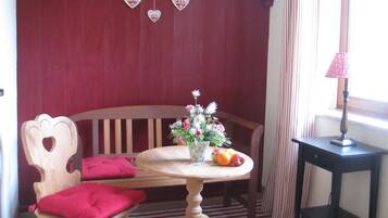 A room with a wooden bench, a table with a vase of flowers and fruit, and a lamp on a side table.