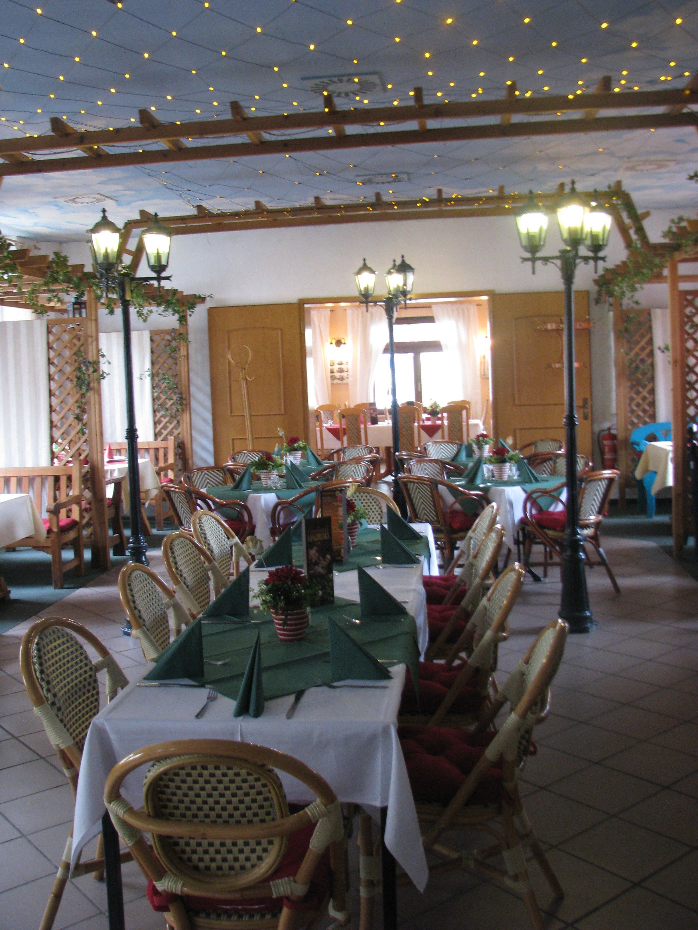 Un restaurant doté de nombreuses tables et chaises, d’un espace extérieur abrité avec des sièges et d’un éclairage décoratif.