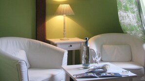Een kamer met twee witte fauteuils, een bijzettafeltje met fles en glas, een lamp en een schilderij aan de muur.