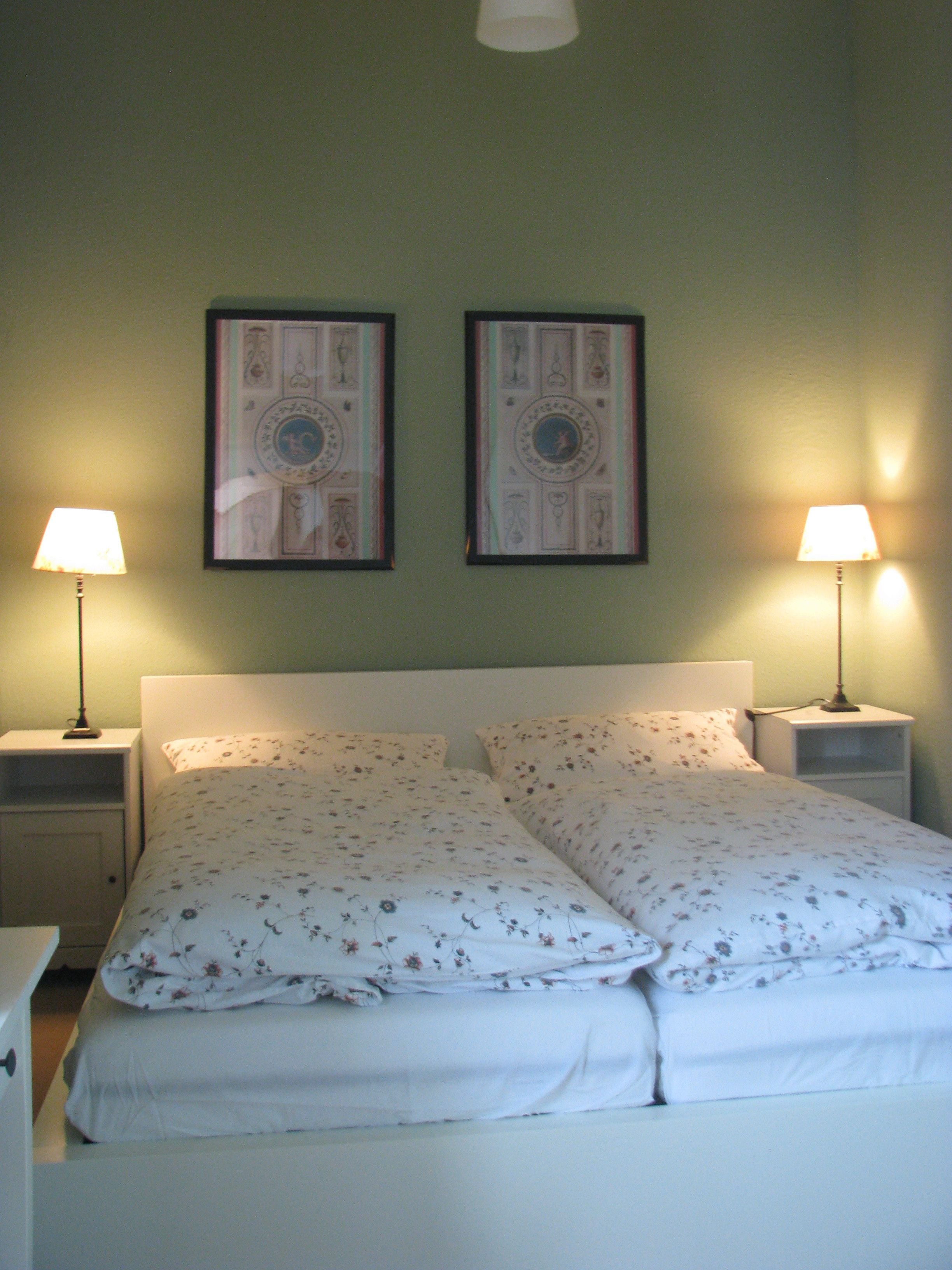 A bed with floral bedding, two bedside lamps, and two framed pictures on the wall.