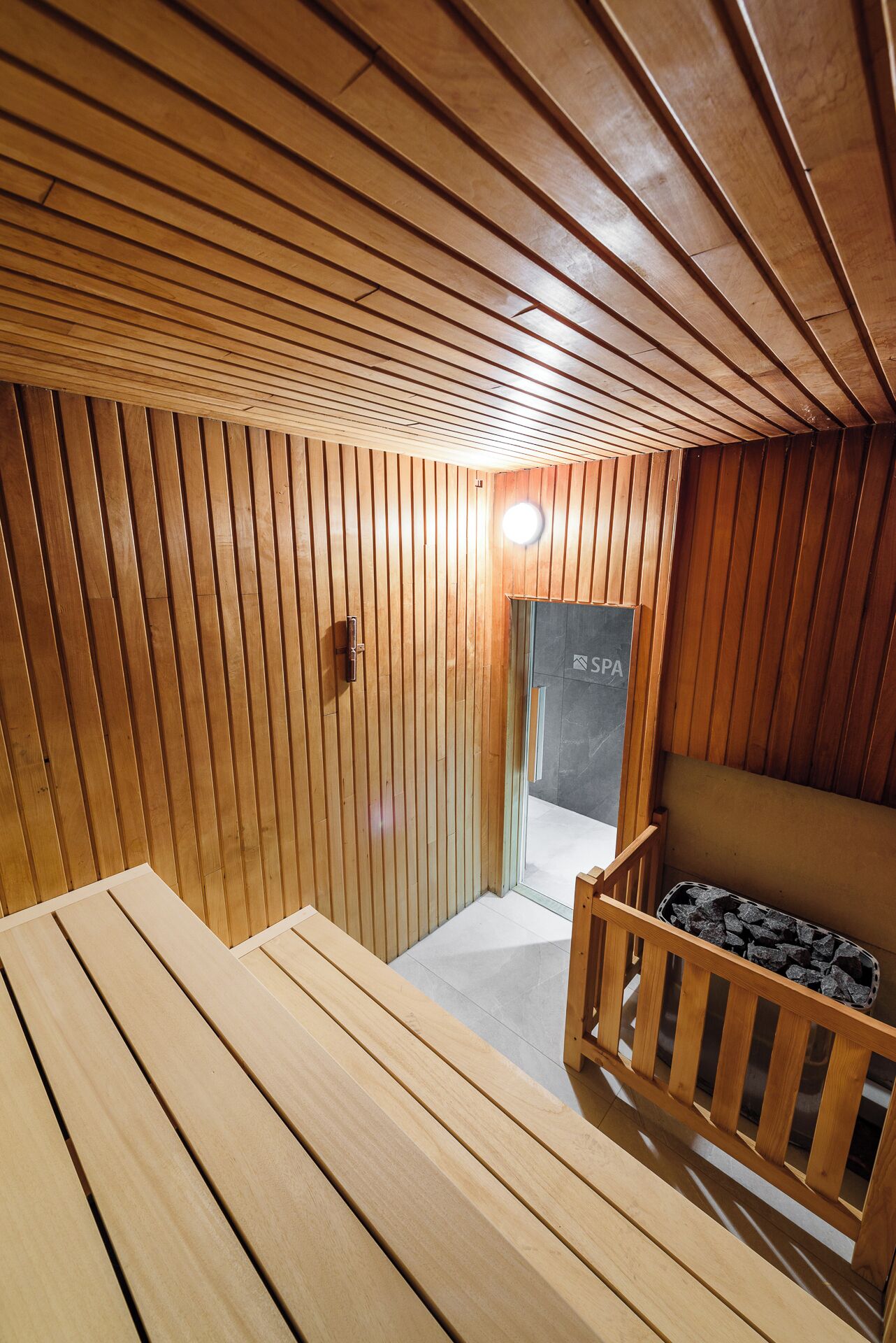 Una sala de sauna con listones de madera en paredes y techo, un banco y un cartel de spa visible a través de la puerta.