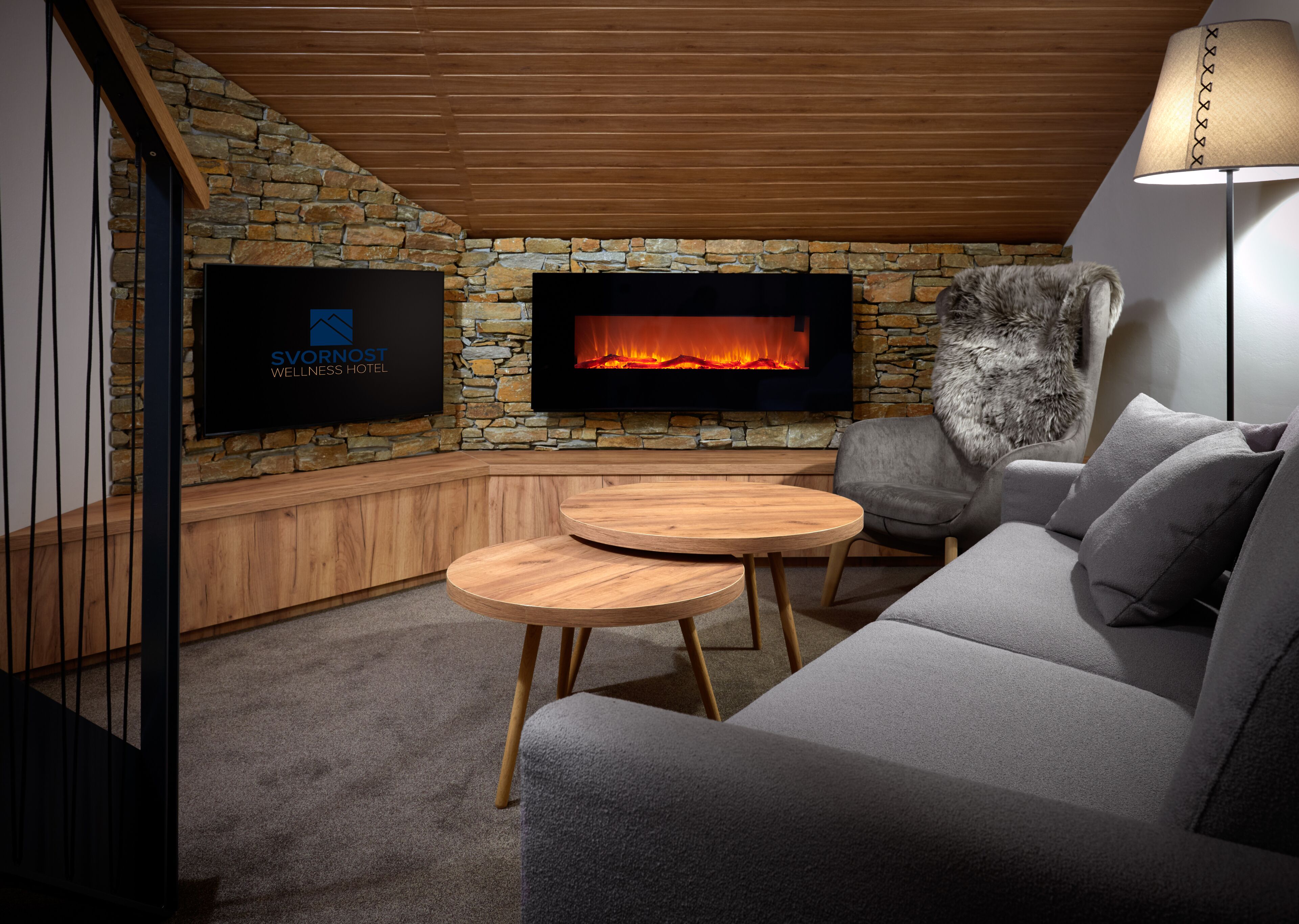 Una habitación acogedora con pared de piedra, chimenea, televisor de pantalla plana, sofá gris y una mesa redonda de madera.