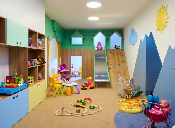 Una sala de juegos infantil con un tobogán, una pared de escalar y diversos juguetes.