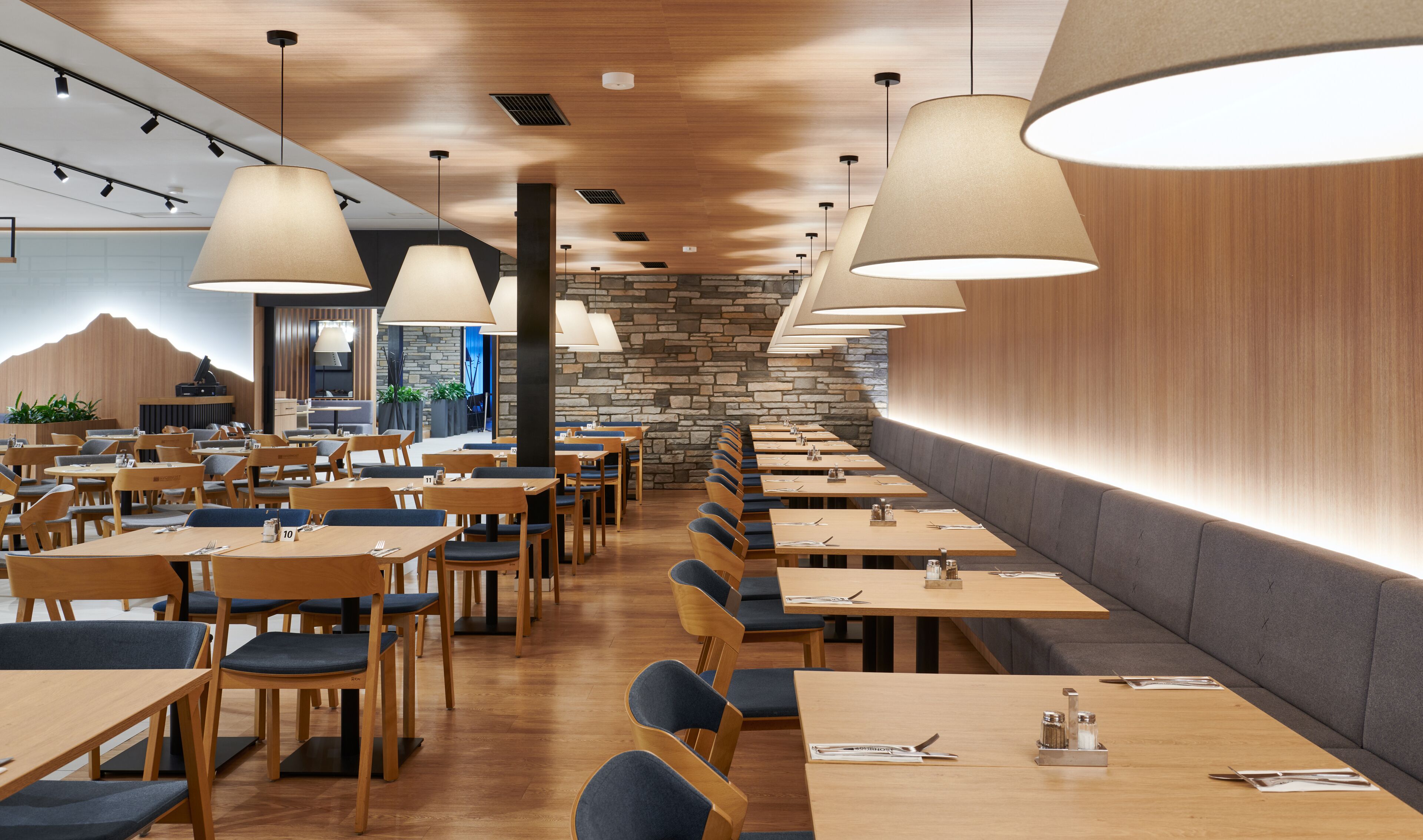 Un restaurante moderno con mesas y sillas de madera, paredes de piedra e iluminación colgante.