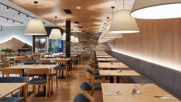 Un restaurante moderno con mesas y sillas de madera, paredes de piedra e iluminación colgante.
