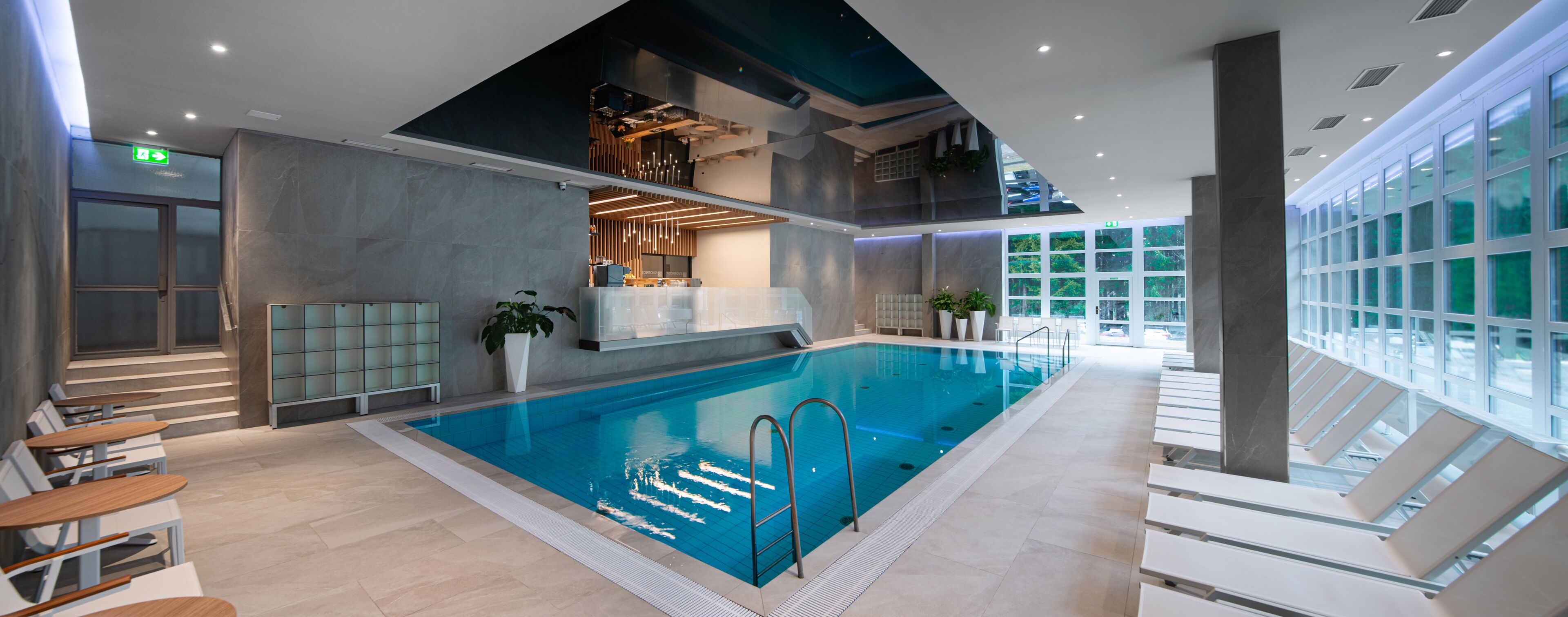 Una piscina interior con diseño moderno, que incluye una terraza con sol y sillones de descanso, y vistas al cielo.