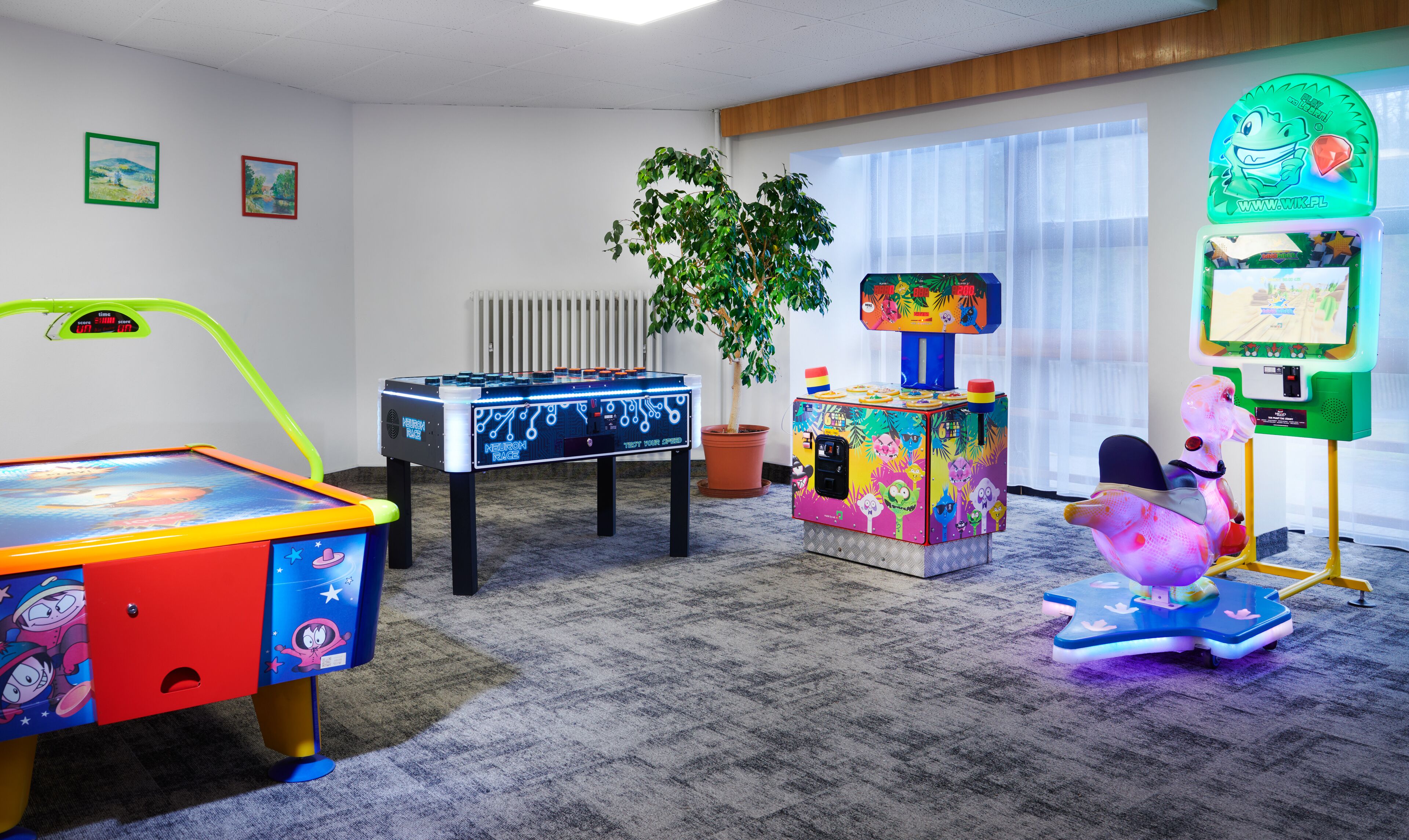 A room with a foosball table, a colorful arcade machine, and a small table with a plant.