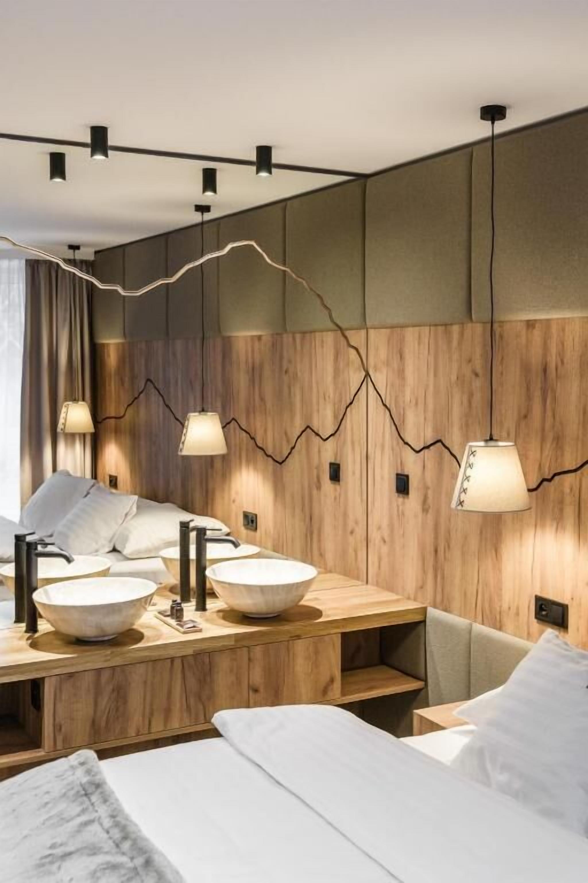 A modern hotel room with a wooden accent wall, a large bed, bedside tables with bowls, and pendant lighting.