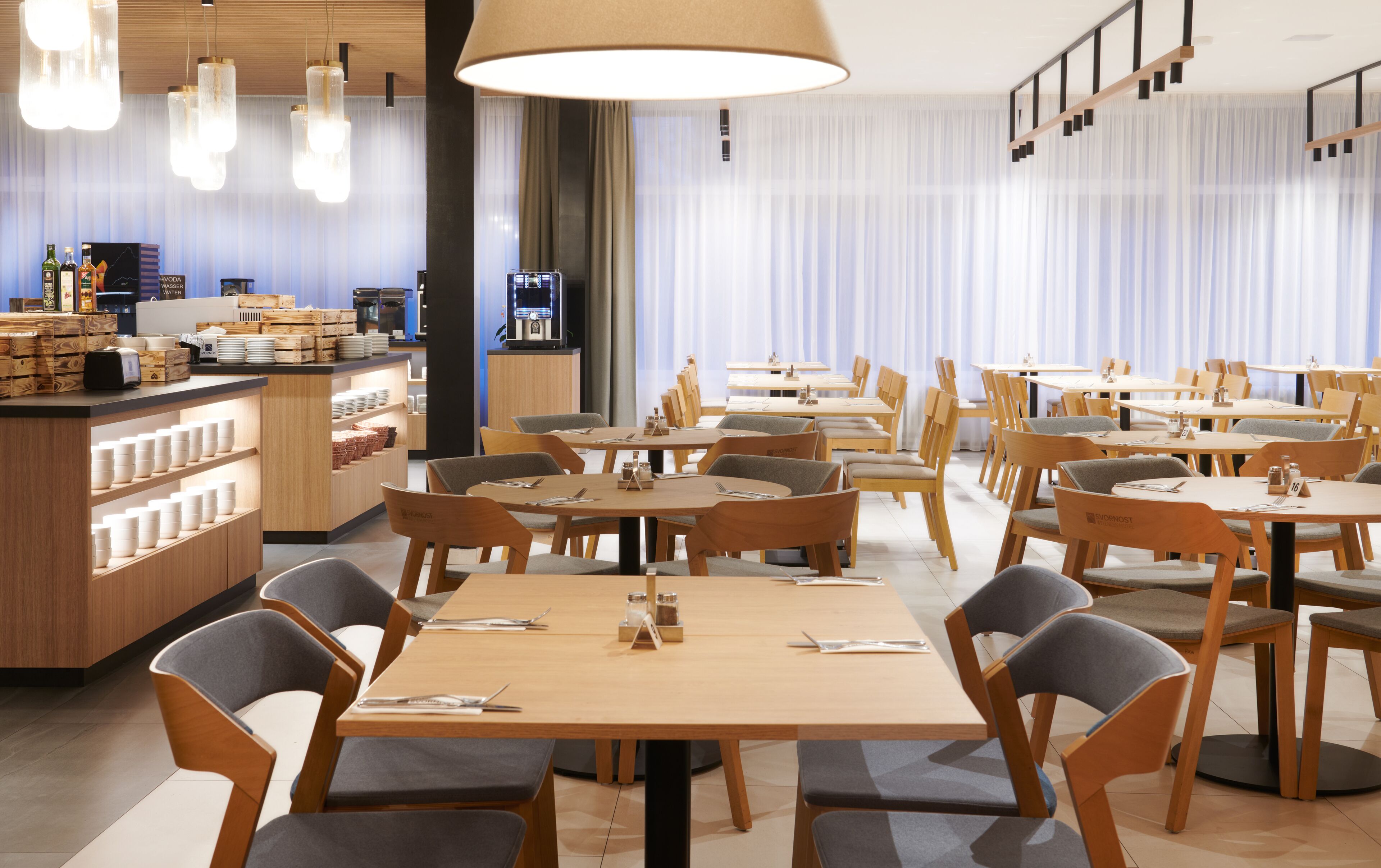 Un ristorante moderno con tavoli e sedie in legno, un'area bar con bottiglie e un'ampia finestra con tende.
