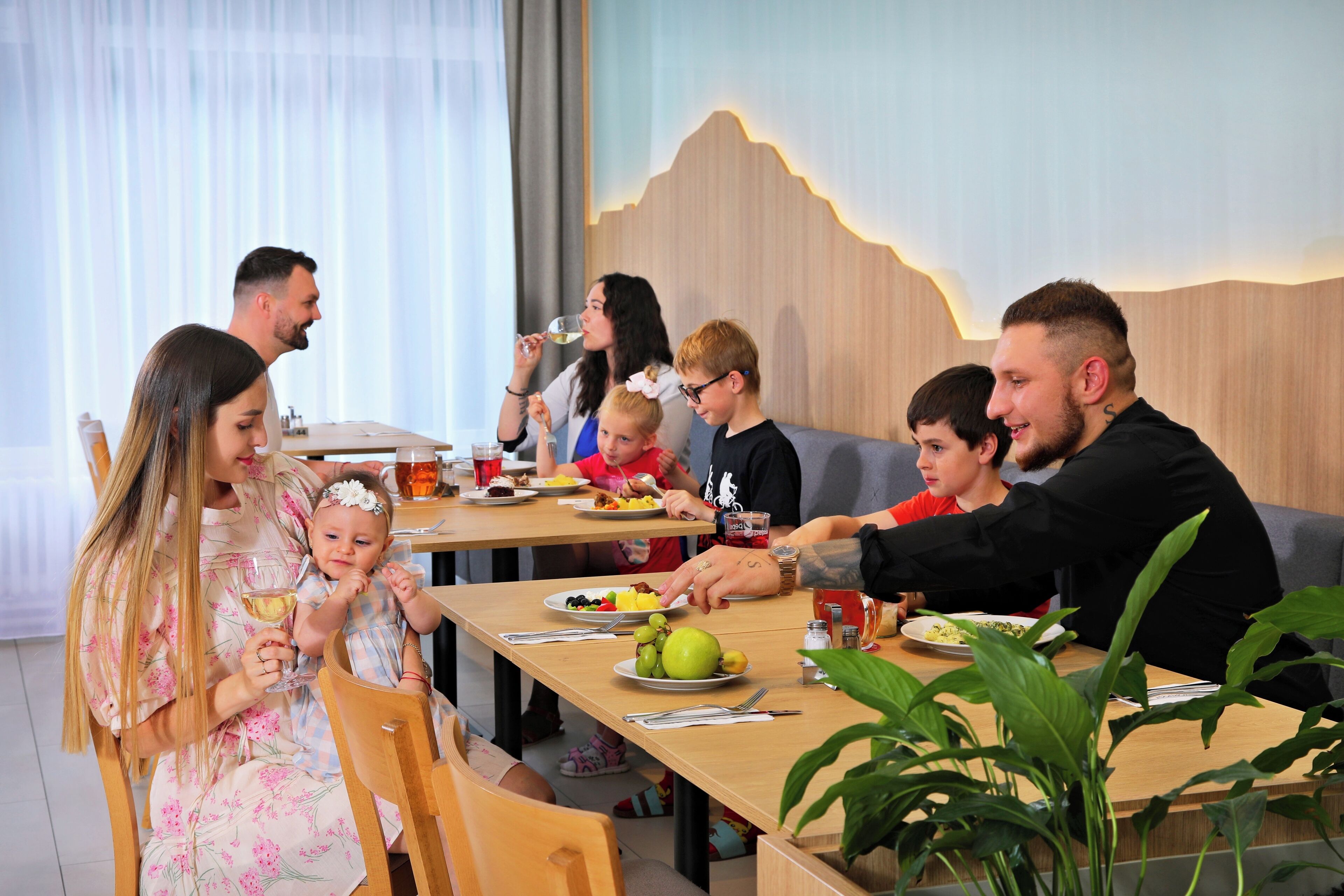 A family dining at a restaurant with a wooden table, chairs, and a mountain-themed wall.
