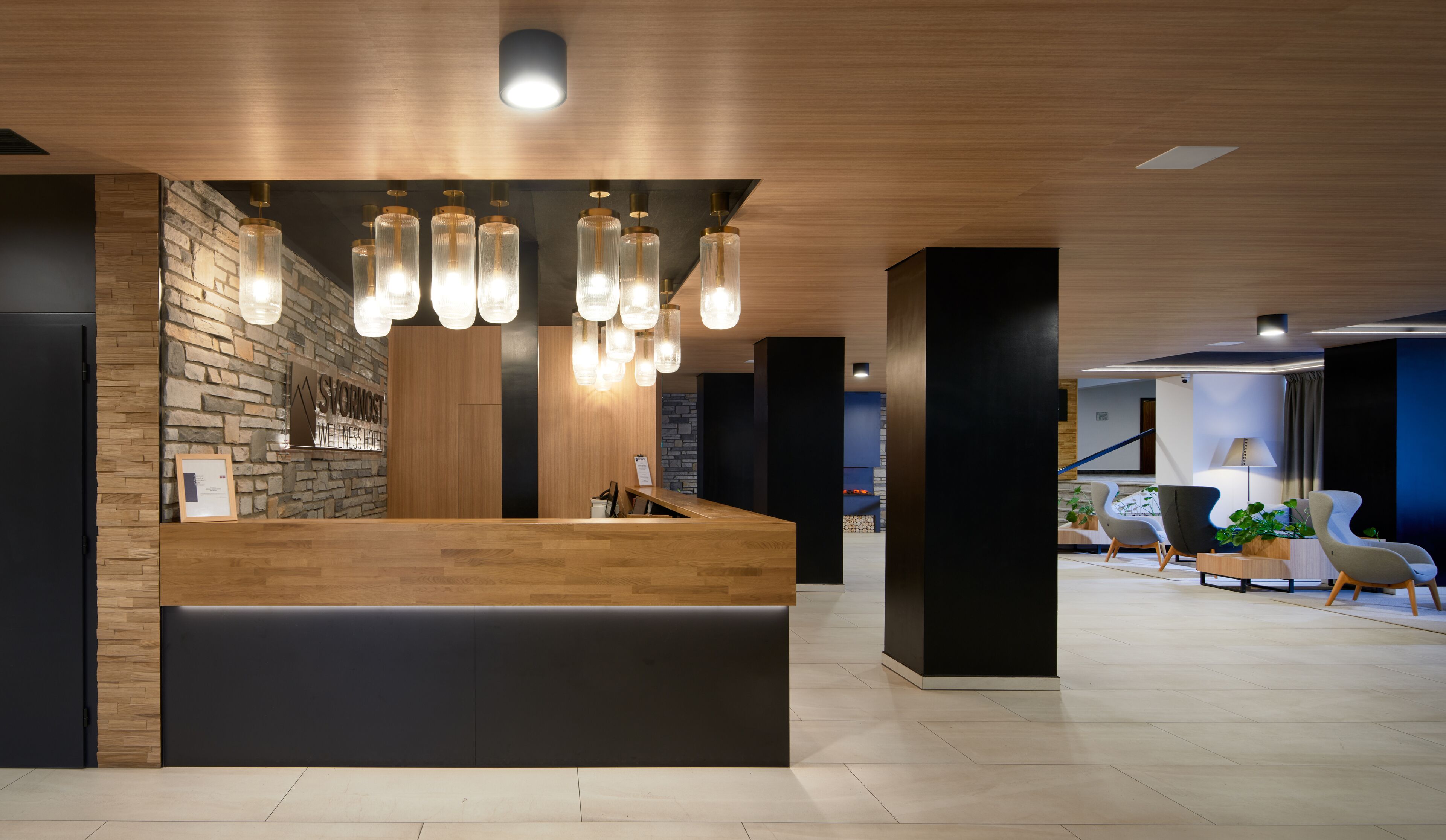 A modern reception desk with a wooden finish, a stone wall backdrop, and hanging pendant lights.