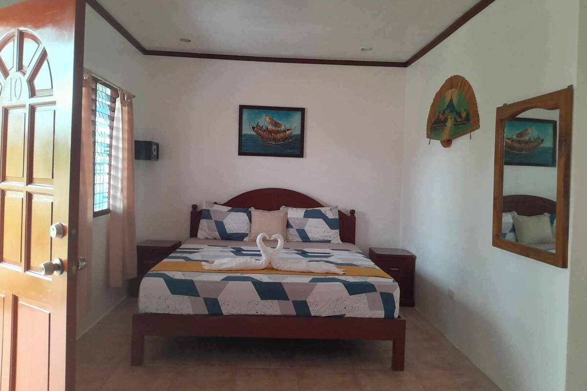 A bedroom with a bed, a nightstand, a door, and two wall-mounted paintings.