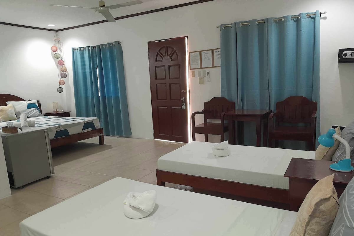 A hotel room with two beds, a desk, a chair, a small table, a ceiling fan, and a door.
