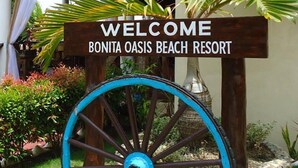 Un panneau d’accueil accueillant les visiteurs du Bonita Oasis Beach Resort, agrémenté d’une roue décorative et de plantes tropicales.