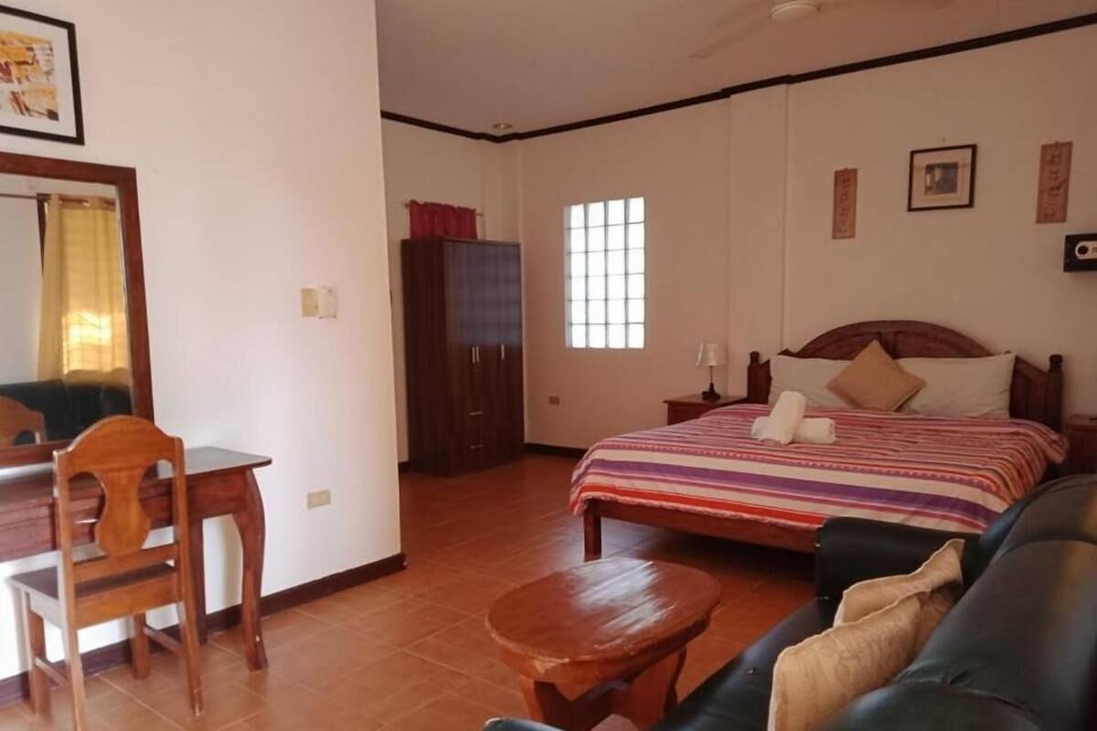 A bedroom with a bed, a wooden desk, a chair, a small table, and a wardrobe.