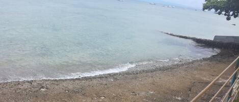 Una playa con agua cristalina y barcos a lo lejos.