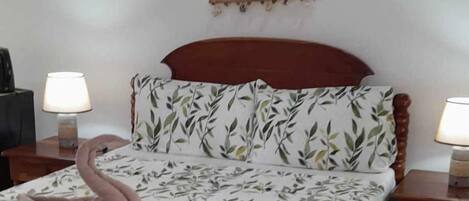 A neatly made bed with a floral bedspread, two bedside lamps, and a wall-mounted net.