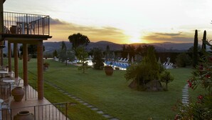 Una terraza con mesas al aire libre y vistas a un jardín ajardinado al atardecer.