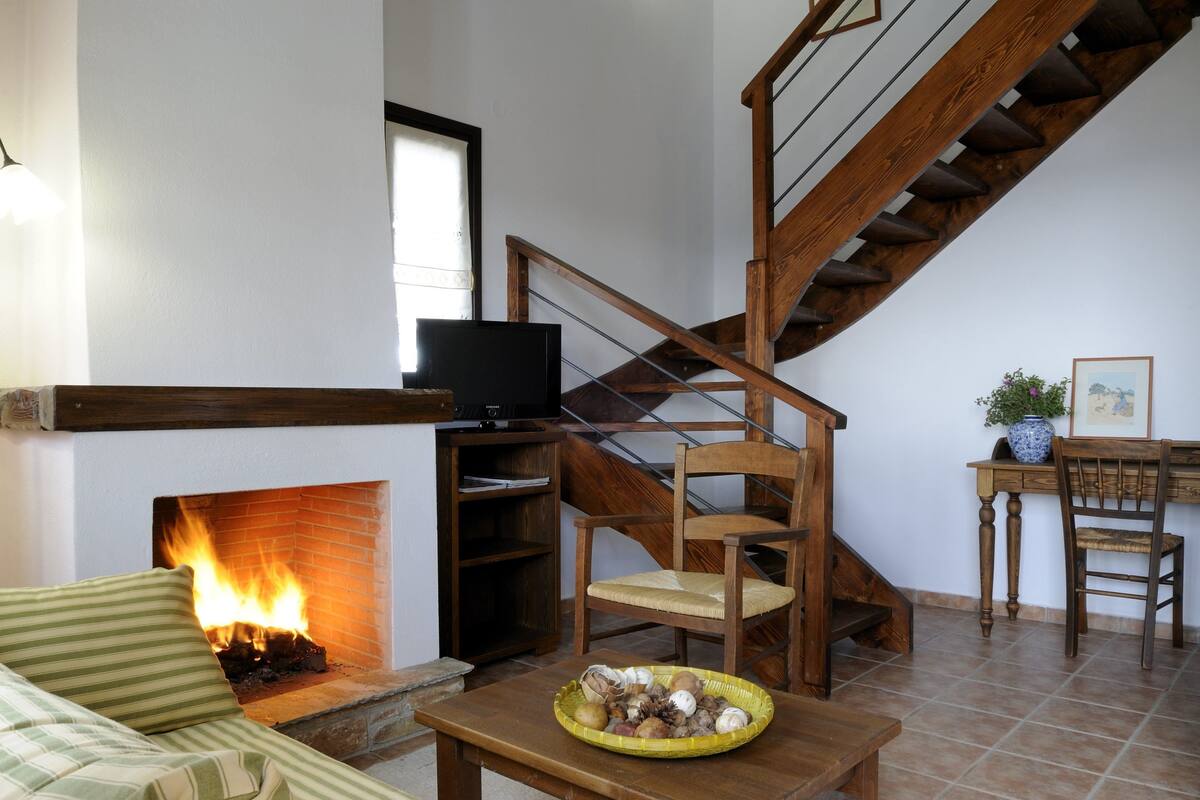 Un salon chaleureux avec une cheminée, un escalier en bois et un téléviseur posé sur une étagère.