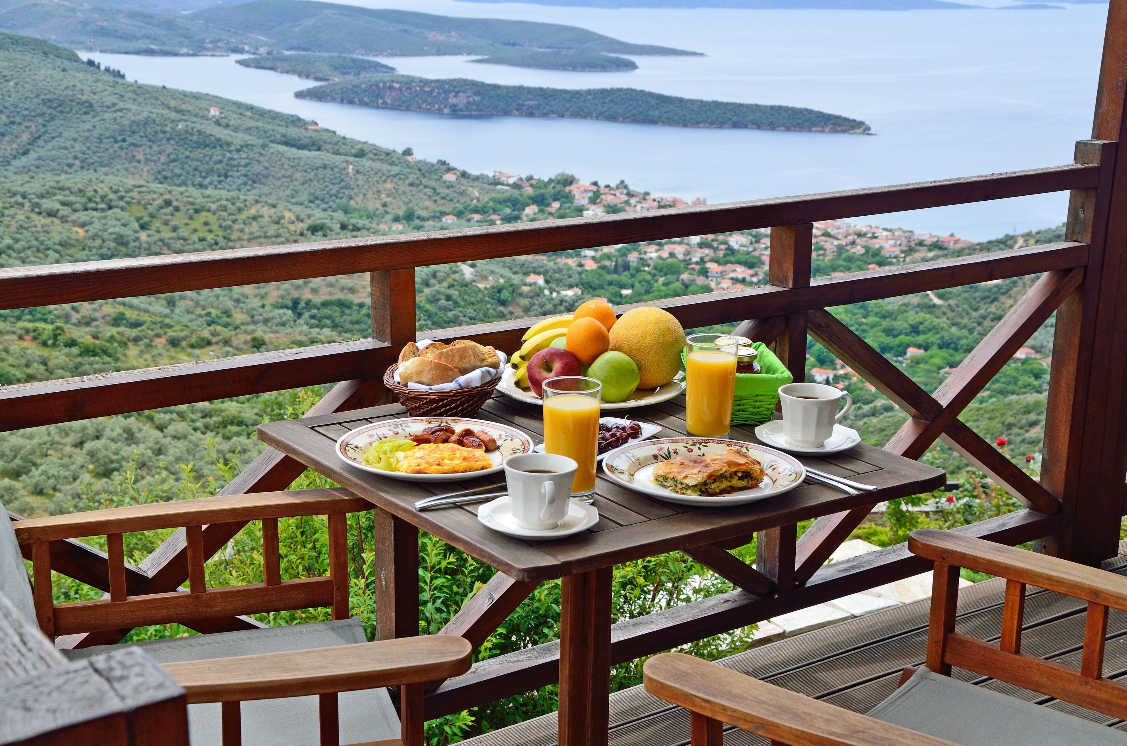 A wooden deck with a table set for breakfast overlooking a scenic lake and hills.
