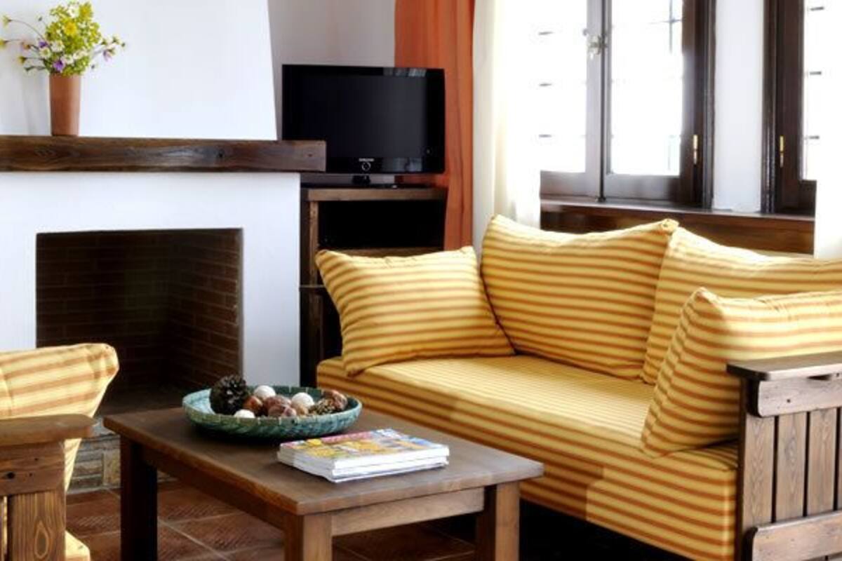 Un salon comprenant un canapé, un fauteuil et une table basse. On y trouve également un téléviseur posé sur un meuble et une cheminée.