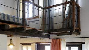 A room with a bunk bed, a sofa, a dining table with chairs, and a window with curtains.