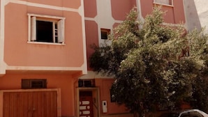 A multi-story building with a pink facade, several windows, and a tree in front. - Khabour Appartment (Safi)