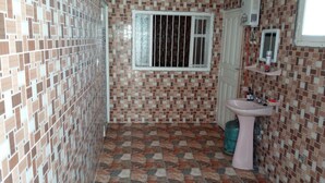A bathroom with a tiled floor and walls, a window with bars, a sink, and a mirror. - Khabour Appartment (Safi)