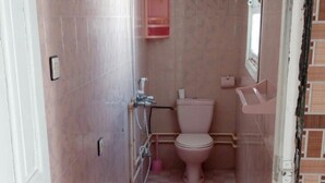 A narrow bathroom with pink tiles, a toilet, a shower area, and a small window. - Khabour Appartment (Safi)
