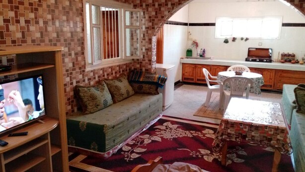 A cozy living room with a sofa, TV, and a dining area with a table and chairs. - Khabour Appartment (Safi)