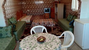 A compact living space with a bed, a small table with a basket, two green sofas, and a white refrigerator. - Khabour Appartment (Safi)