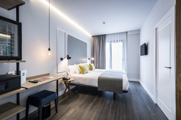 A modern hotel room with a bed, desk, and TV.