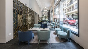 Et moderne interiør med et geometrisk vægdesign, siddeområde med borde og store vinduer med udsigt til gaden.